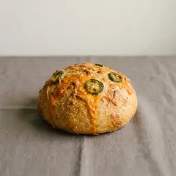 Kerek sajtos kenyér, a héján rásült cheddar és néhány jalapeno karika.